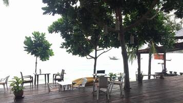 An outdoor seating area with wooden flooring, chairs, and tables, overlooking a body of water.