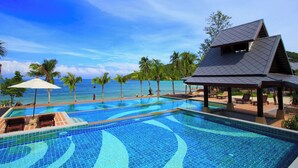 Ein Swimmingpool mit klarem, blauem Wasser, umgeben von Liegestühlen und Sonnenschirmen, mit Blick auf den Ozean und Palmen.