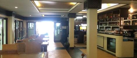 A hotel lobby with a reception desk, a bar area, and a seating area with wicker furniture.