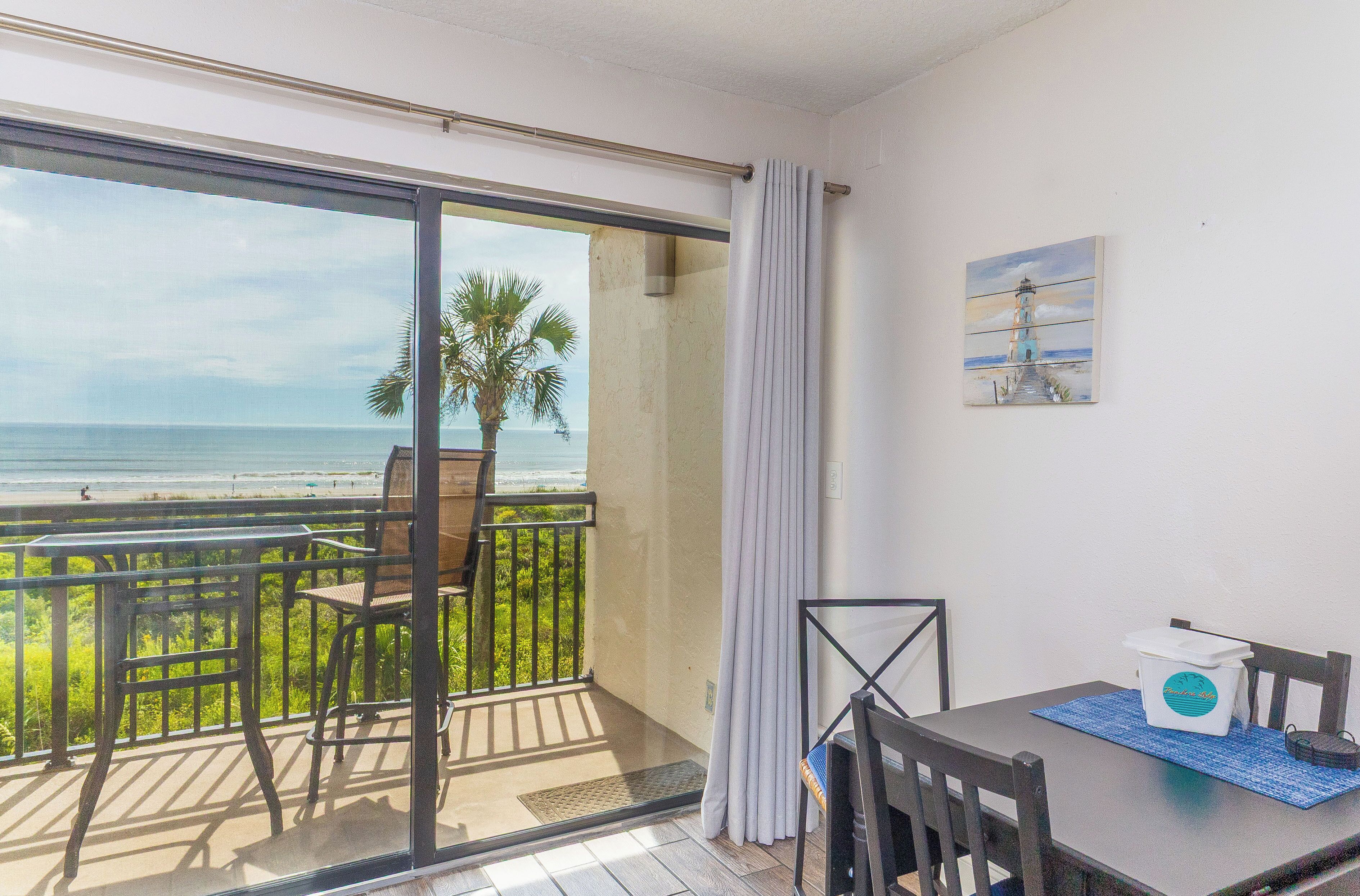 A balcony with a view of the ocean, a table with chairs, and a painting on the wall.