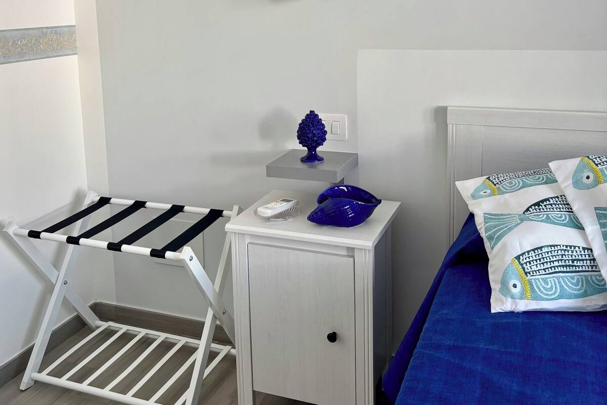 A bedroom with a bed, a nightstand, a wall-mounted light, and a drying rack.