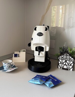 Una macchina da caffè con montalatte, una tazza e un piattino, un portacarte e un oggetto decorativo a forma di casetta su un tavolo.