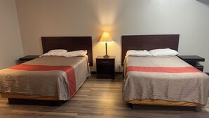 Et hotelværelse med to enkeltsenge, trægavle, et natbord med lampe og trægulv.