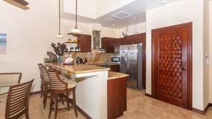 A modern kitchen with a central island, stainless steel appliances, and wooden cabinetry. - Pristine Bay 1205 2 Bedroom Villa (Roatan)