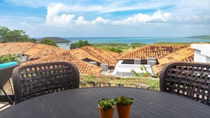 A rooftop terrace with a view of the ocean, featuring a table with chairs and potted plants. - Pristine Bay 1205 2 Bedroom Villa (Roatan)