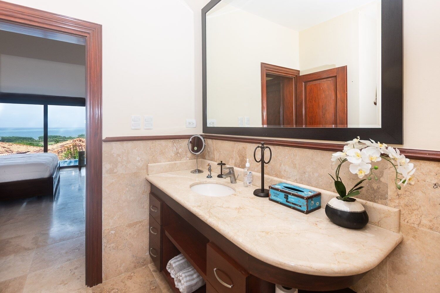 A bathroom with a large mirror, two sinks, a vanity, and a view of the outdoors.