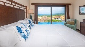 A hotel room with a large bed, a view of the sea, and a chair by the window. - Pristine Bay 1205 2 Bedroom Villa (Roatan)