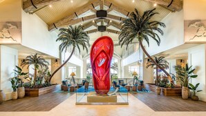 A spacious lobby with a central red sculpture, wooden ceiling beams, and palm trees. - Paradise Breeze Cottage By Shine Villas Margaritaville Resort Orlando 4 Bedroom Condo (Kissimmee)