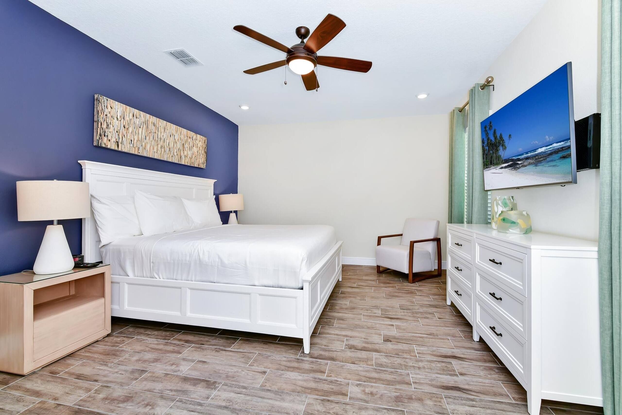 A bedroom with a bed, nightstands, a dresser, a ceiling fan, and a TV on the wall.