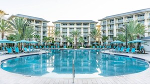 A hotel pool area with a central pool, lounge chairs, and umbrellas. - Paradise Breeze Cottage By Shine Villas Margaritaville Resort Orlando 4 Bedroom Condo (Kissimmee)