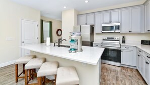 A modern kitchen with white cabinets, a central island with bar stools, a built-in oven, and a microwave. - Paradise Breeze Cottage By Shine Villas Margaritaville Resort Orlando 4 Bedroom Condo (Kissimmee)