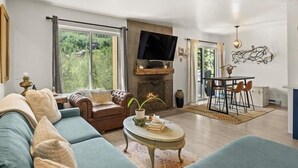 A living room with a sofa, a coffee table, a fireplace, a TV, and a dining area with chairs and a table. - Remodeled Snowmass Pet-Friendly Modern 1BR Condo - G125 (Snowmass Village)