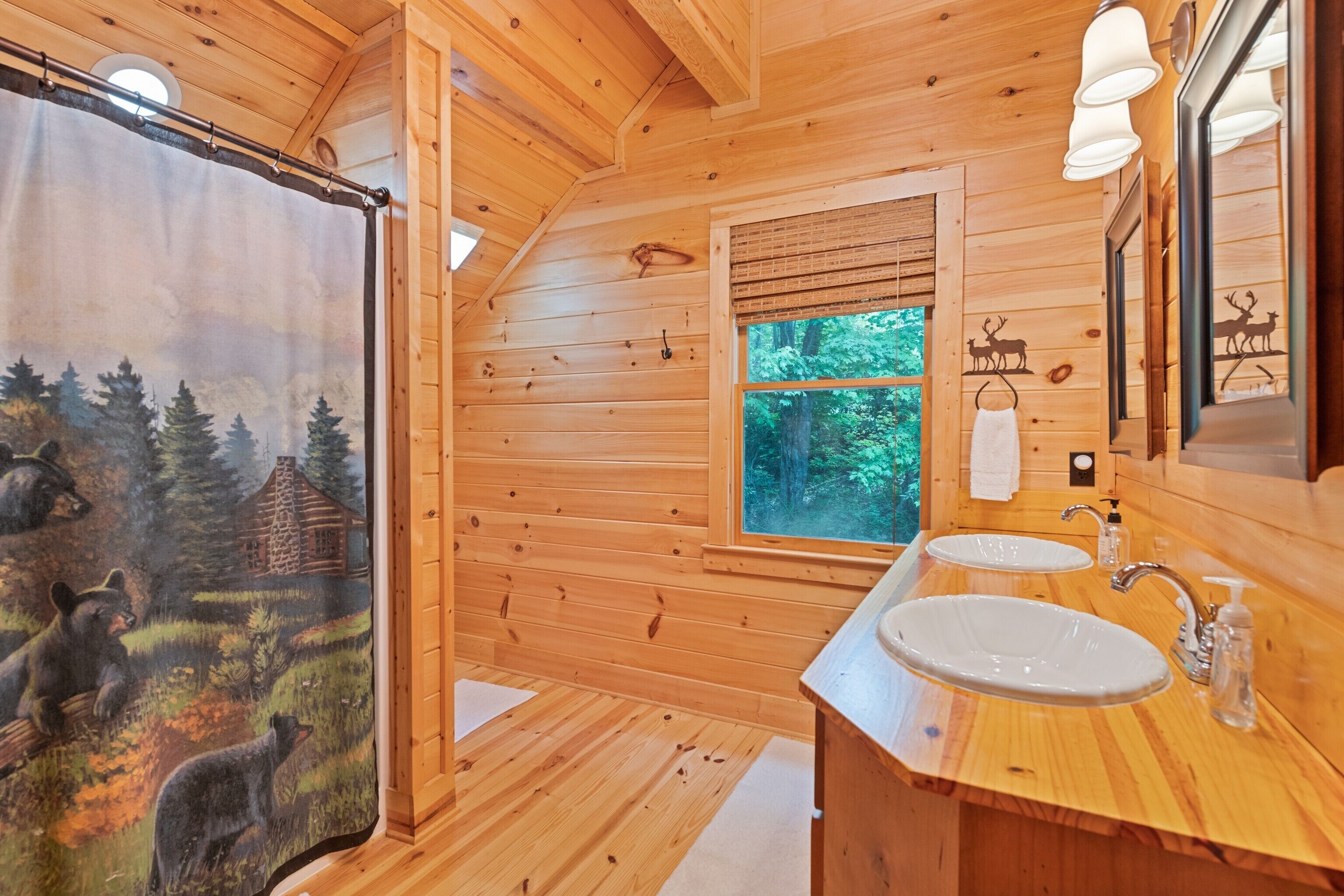 A wooden cabin bathroom with two sinks, a window with a view of the forest, and a bear mural on the wall.