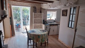 A cozy kitchen with a round table, wooden cabinets, and a view of the garden through the door.