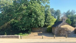 A stone building with a thatched roof, surrounded by trees and a stone wall.