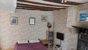A bedroom with a stone wall, a bed with a purple bedspread, a wooden bench, a bookshelf, a TV, and a fireplace.