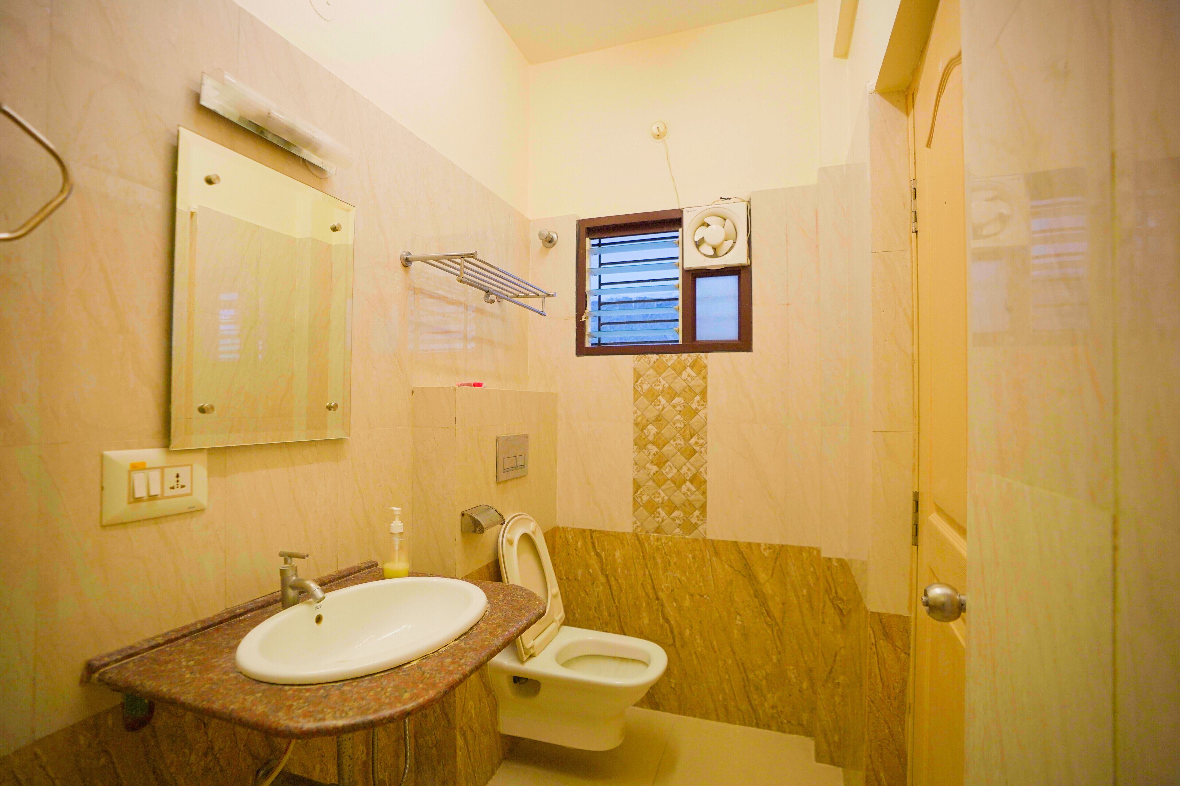 Un baño con lavamanos, inodoro, espejo, toallero y ventana con persianas.