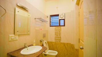 Un baño con lavamanos, inodoro, espejo, toallero y ventana con persianas.
