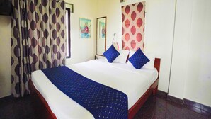 A hotel room with a bed, curtains, a painting, and a window with a patterned curtain. - Mystic Felicity Inn (Bengaluru)