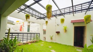 A covered outdoor area with a green lawn, hanging plants, and a door leading to an interior space. - Mystic Felicity Inn (Bengaluru)