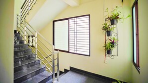 A staircase with metal railings, a window with horizontal bars, and a wall-mounted plant holder with multiple plants. - Mystic Felicity Inn (Bengaluru)