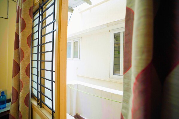 A window with a metal grid, a view of a building outside, and a curtain with a circular pattern.