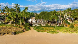 Una propiedad frente a la playa con un sendero arenoso que conduce a un edificio con varios balcones con vistas al mar.