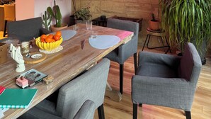 Un coin repas avec une table en bois, des chaises à revêtement gris et un panneau lumineux au néon sur le mur.