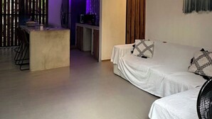 Una sala moderna con un sofá, una zona de comedor con una mesa y una cocina al fondo.