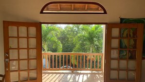 Une chambre avec un balcon, des portes en bois et un sol carrelé.