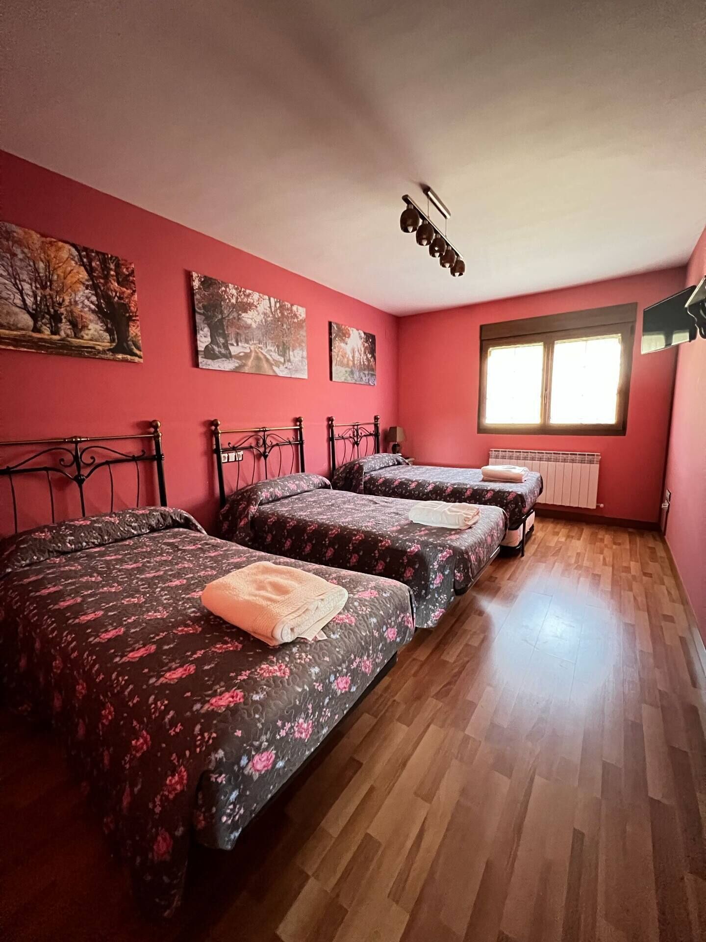 Una habitación con tres camas, una ventana y obras de arte en las paredes.