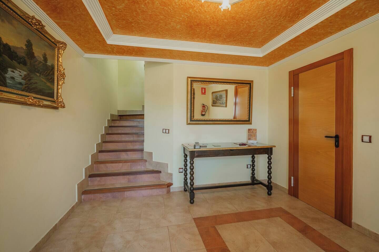 A hallway with a staircase, a wooden door, a framed picture, and a small table with a mirror.