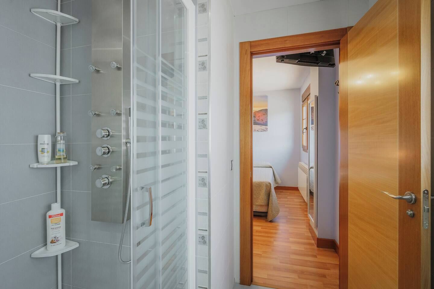 Une salle de bain moderne avec une douche à parois de verre, une porte en bois et un couloir menant à une chambre.