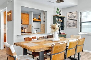 A dining area with a rustic wooden table, leather chairs, and a vase with dried flowers.