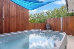 A hot tub in a backyard with wooden fences and a blue canopy.