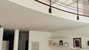 Tilava olohuone, jossa on korkea katto, kattovalaisin, portaikko ja valkoinen sohva.