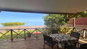 A wooden deck with a table and chairs, overlooking a body of water and a small island.