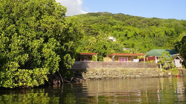 A coastal property with a stone wall, two buildings with red roofs, and lush greenery.