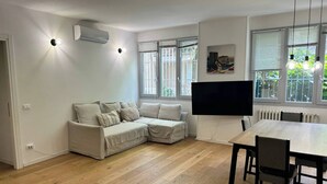 A modern living room with a sectional sofa, a dining table, and a flat-screen TV. - 3 rooms equipped all comfort with swimming pool and tennis near the navigli (Milano)
