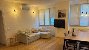 A living room with a sofa, a TV, a dining table with chairs, and a radiator. - 3 rooms equipped all comfort with swimming pool and tennis near the navigli (Milano)