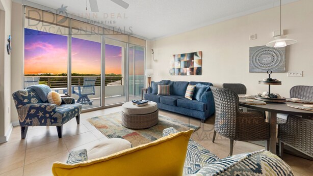 A modern living room with a blue sofa, yellow armchair, and a dining area with wicker chairs. - Ocean Club 401 | Enjoy Views of the Gulf! (Biloxi)