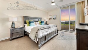 A bedroom with a bed, nightstands, a ceiling fan, and a large window with a view. - Ocean Club 401 | Enjoy Views of the Gulf! (Biloxi)