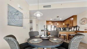 A dining area with wicker chairs, a round table, and a decorative centerpiece. - Ocean Club 401 | Enjoy Views of the Gulf! (Biloxi)