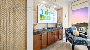 A modern living room with a wooden cabinet, a flat-screen TV, and a blue armchair with a nautical theme. - Ocean Club 401 | Enjoy Views of the Gulf! (Biloxi)