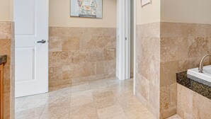 A bathroom with beige tiles, a white door, and a sink with a granite countertop. - Ocean Club 401 | Enjoy Views of the Gulf! (Biloxi)