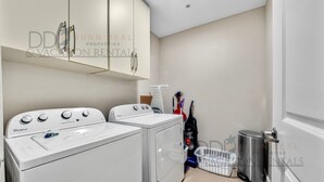 A laundry area with two white Whirlpool washers and dryers, a metal trash can, and a laundry basket.