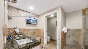 A modern bathroom with a granite sink, a toilet, and a shower area.