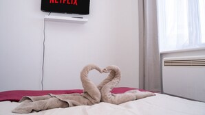 Ein Hotelzimmer mit Bett, einem an der Wand montierten Fernseher, der 'NETFLIX' anzeigt, und einem Fenster mit Vorhängen.