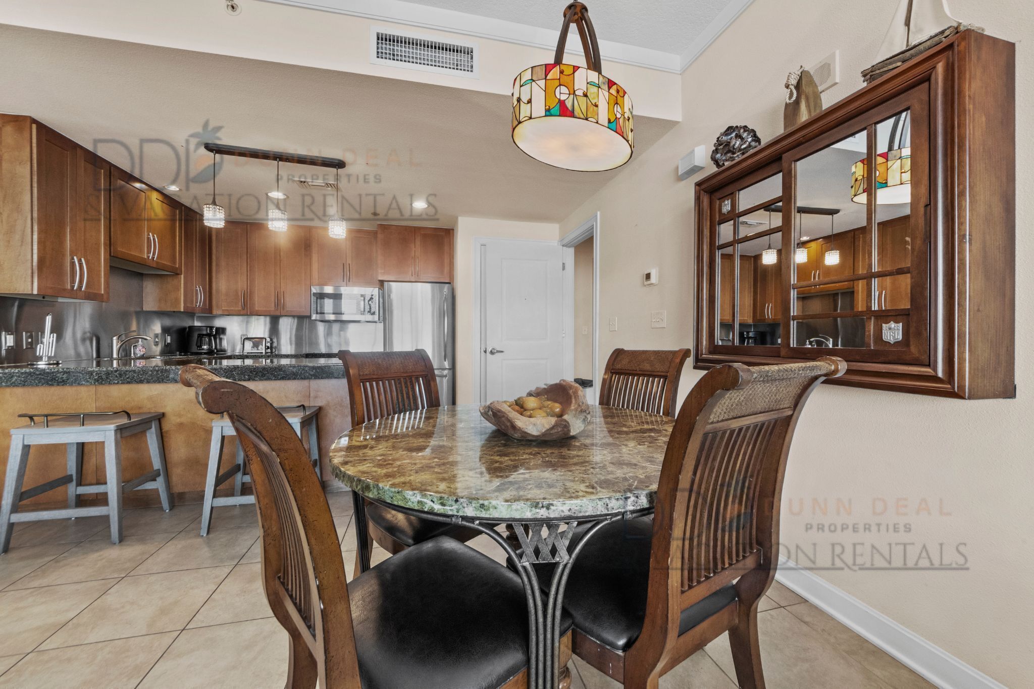A modern kitchen with granite countertops, stainless steel appliances, and wooden cabinets. There is a dining area with a marble table and wooden chairs.