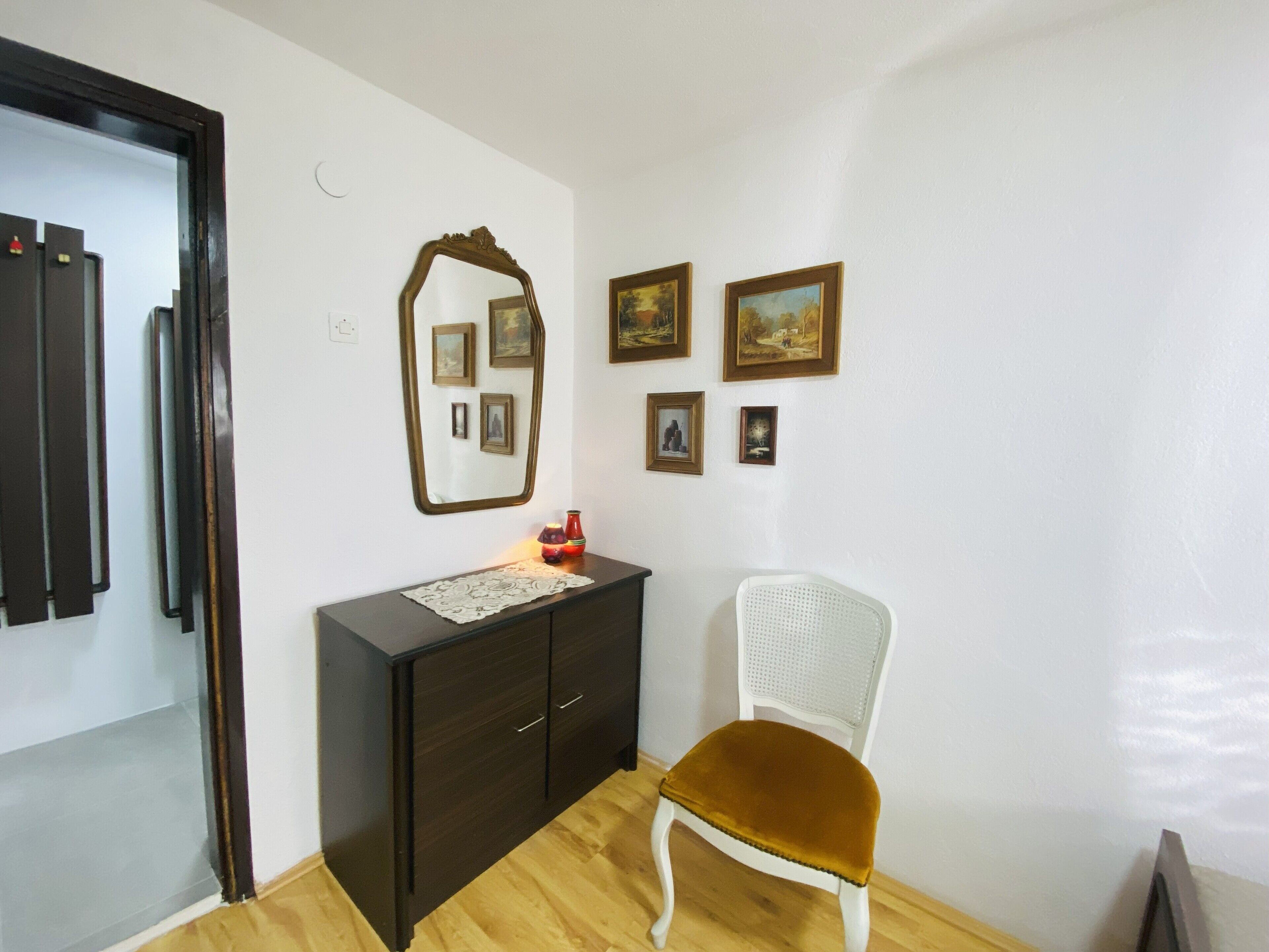 A room with a dark wooden cabinet, a white chair with a brown cushion, and several framed pictures on the wall.
